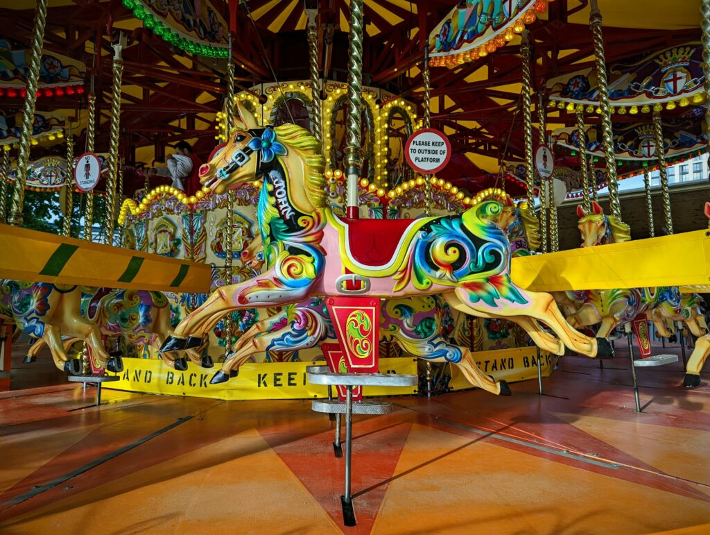 A brightly painted ornate carousel horse decorated with vibrant pink, yellow, and blue swirls on a traditional funfair merry-go-round.