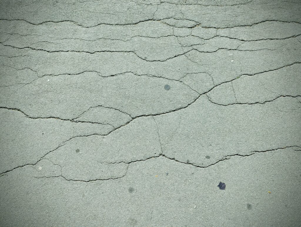 Horizontal cracks and fissures spread across a weathered grey asphalt surface with a dark vignette around the edges.