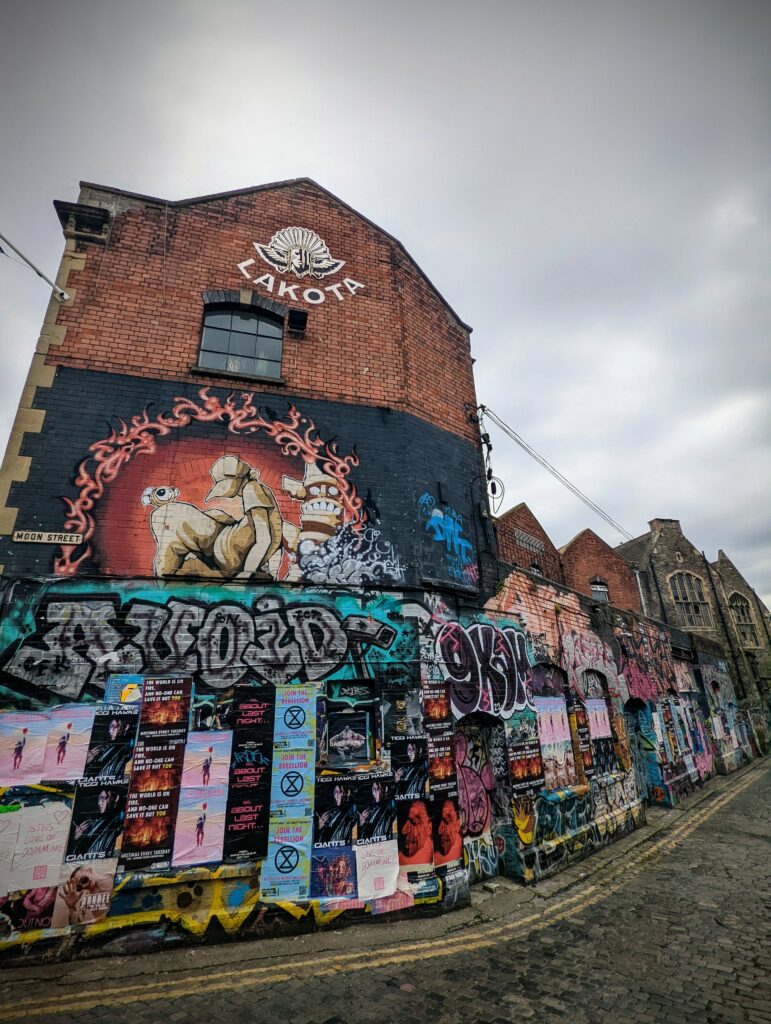Vibrant graffiti and posters cover the base of the red brick Lakota nightclub building on Moon Street under an overcast sky.