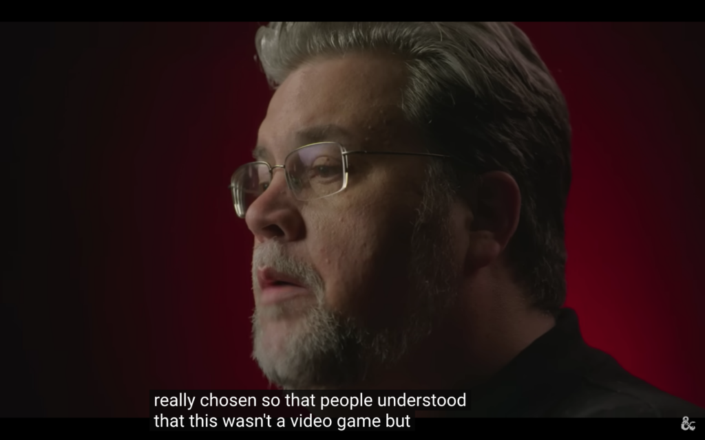Screenshot of a Dungeons & Dragons video featuring a man with a beard and glasses in profile against a red background. Subtitles read: really chosen so that people understood that this wasn't a video game but.