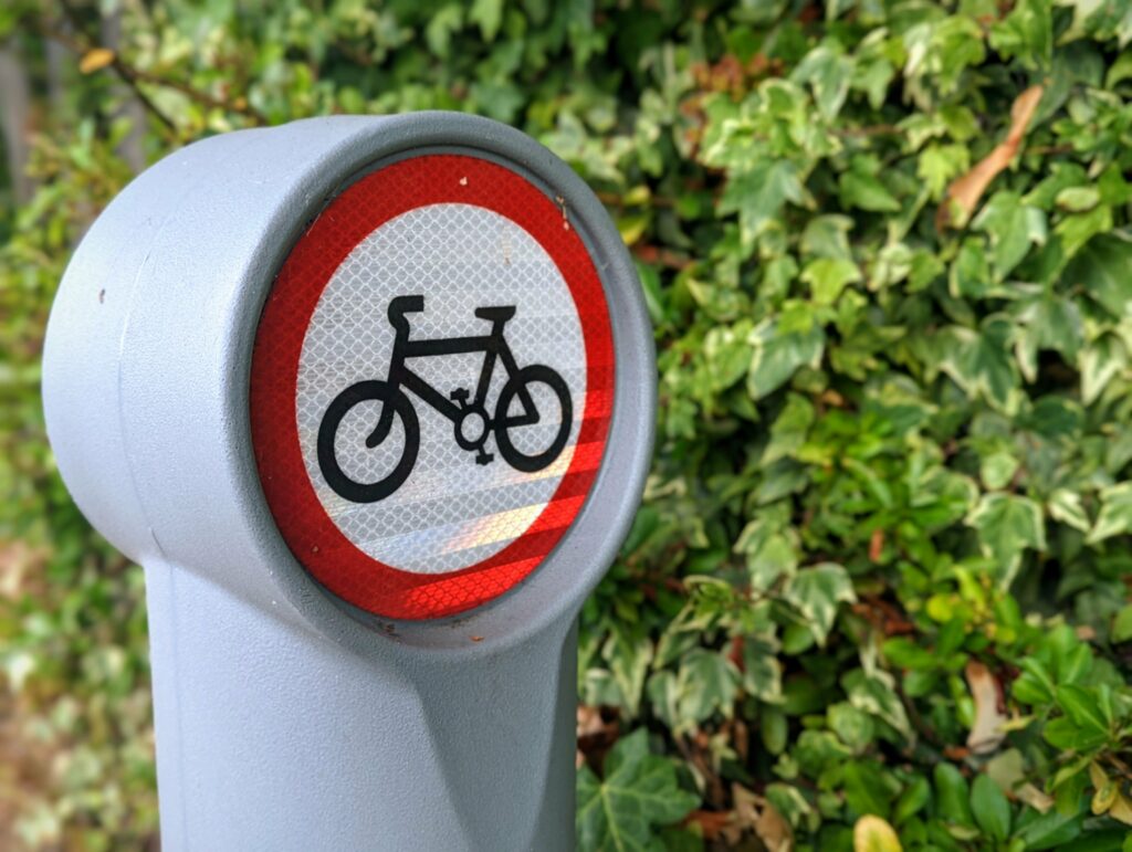 A reflective no cycling sign on a grey plastic bollard against a dense green ivy hedge.