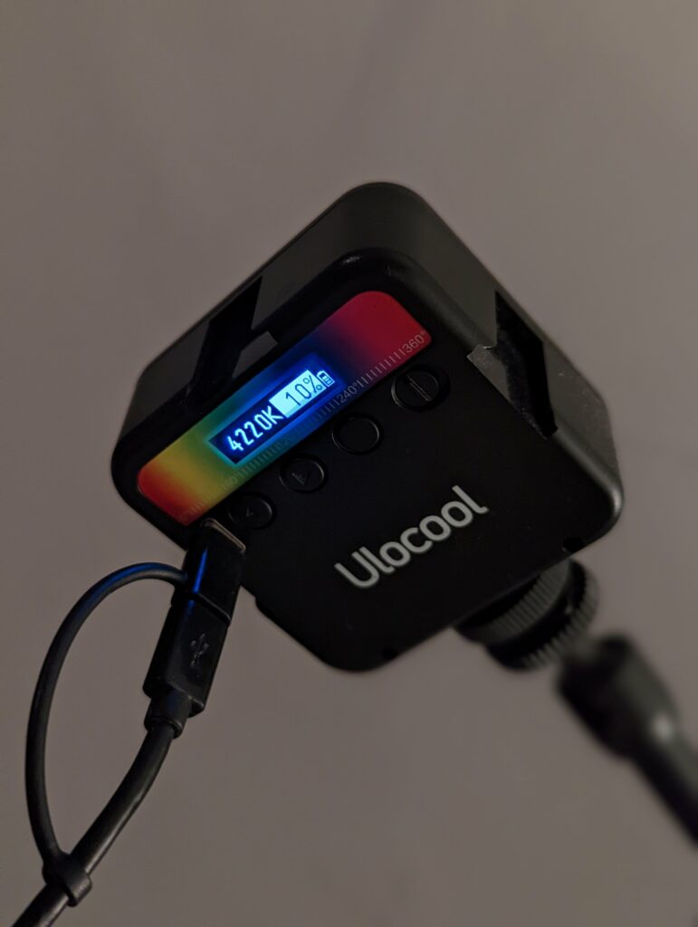 A black Ulocool portable LED light mounted on a stand, showing 4220K and 10% brightness on a small digital display while charging via USB.