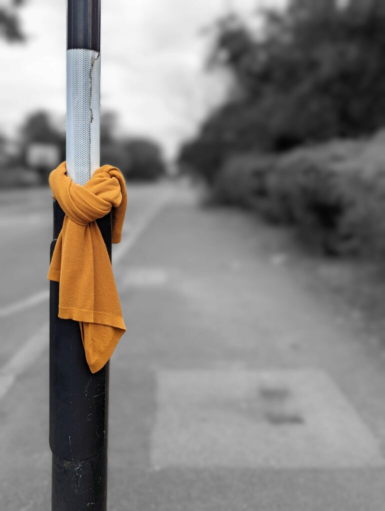 A mustard yellow scarf knotted around a black street pole in selective color against a blurred grayscale background.