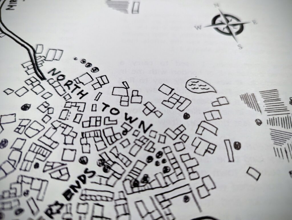 Hand-drawn black ink map of North Town on white paper, showing clusters of small buildings, a compass rose, and a small pond.