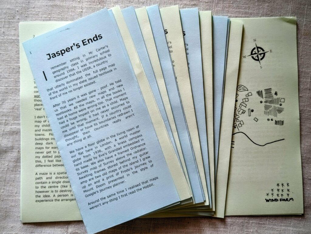 A stack of fanned blue and cream pamphlets titled Jasper’s Ends, one featuring a hand-drawn map and compass rose illustration.