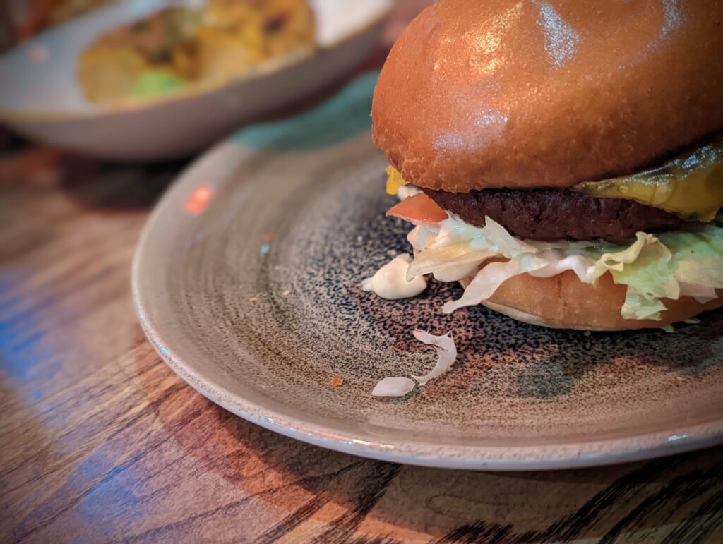 A cheeseburger with lettuce, tomato, and mayo on a glossy brioche bun, served on a speckled grey plate on a wooden table.