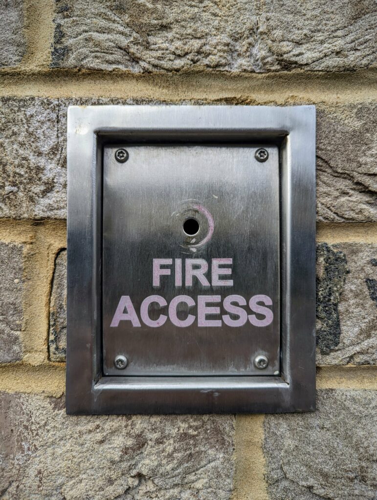 Brushed metal FIRE ACCESS panel with a central keyhole set into a textured stone wall.