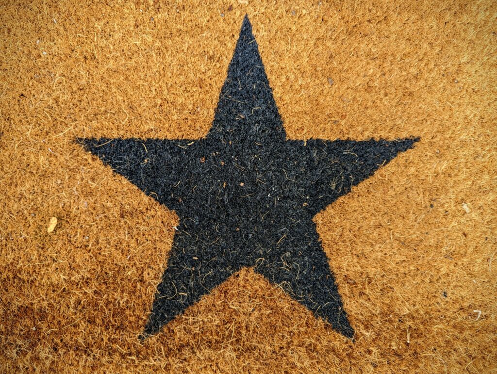 A black five-pointed star printed on the coarse, fibrous surface of a tan-colored coir doormat.