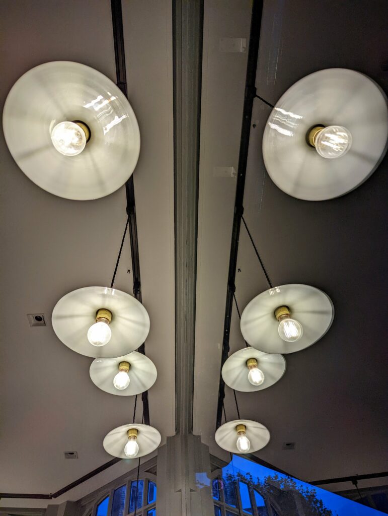Symmetrical reflection of white saucer-shaped pendant lights with glowing bulbs hanging from black tracks on a ceiling.