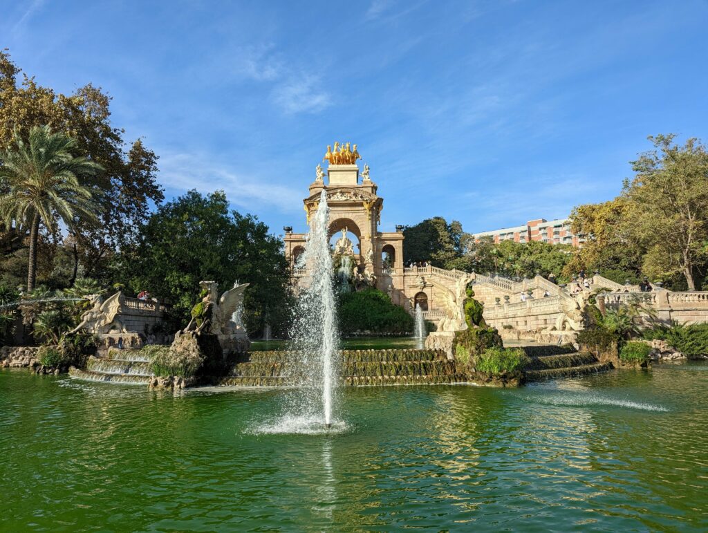The Cascada Monumental fountain in Barcelona featuring golden statues and stone dragons spraying water into a large pond under a blue sky.