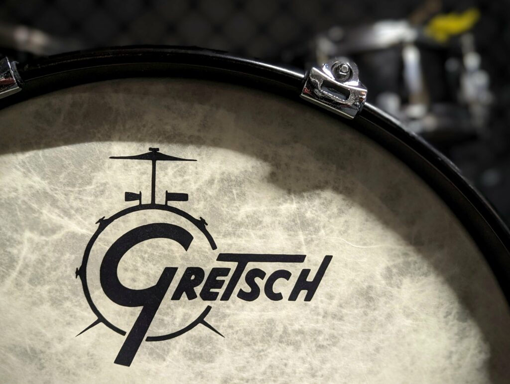 A close-up of the Gretsch logo on a textured off-white drum head with a black rim and metal hardware.
