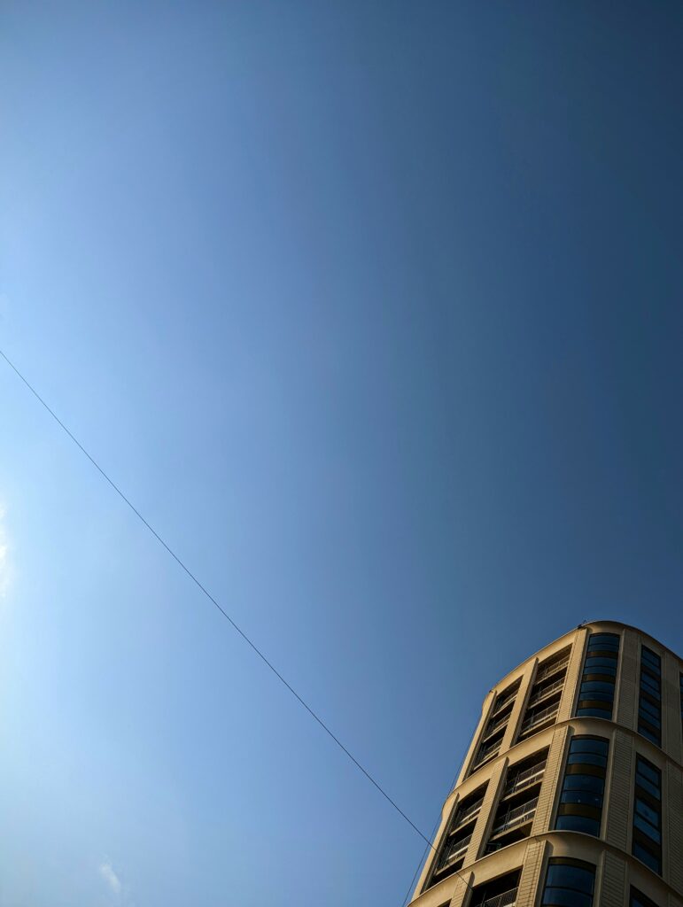 A modern rounded apartment building in the lower right corner set against a vast, clear blue sky with a single thin diagonal wire.