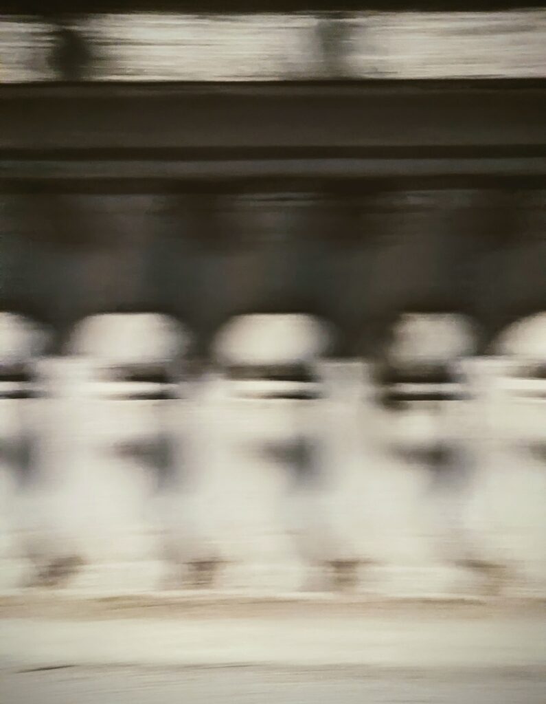 Abstract horizontal motion blur of a row of white stone bollards against a dark background.