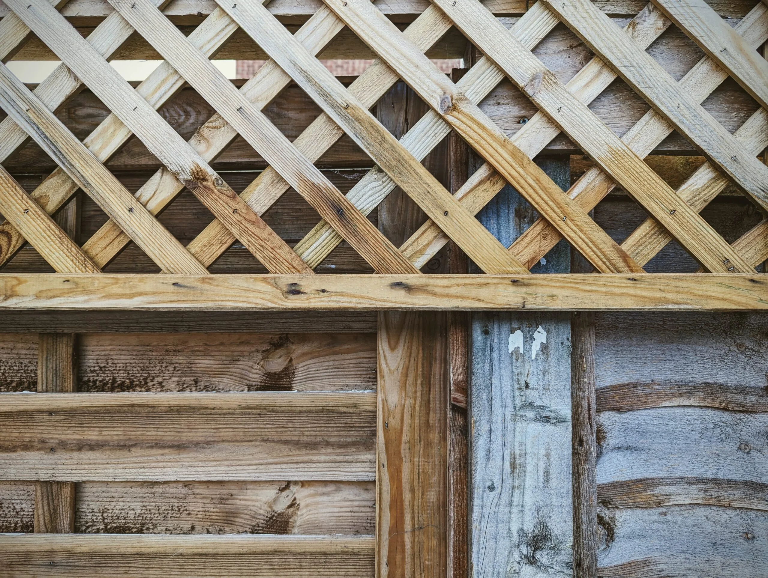 Wooden garden fence featuring a diamond-patterned trellis top above weathered horizontal timber panels.