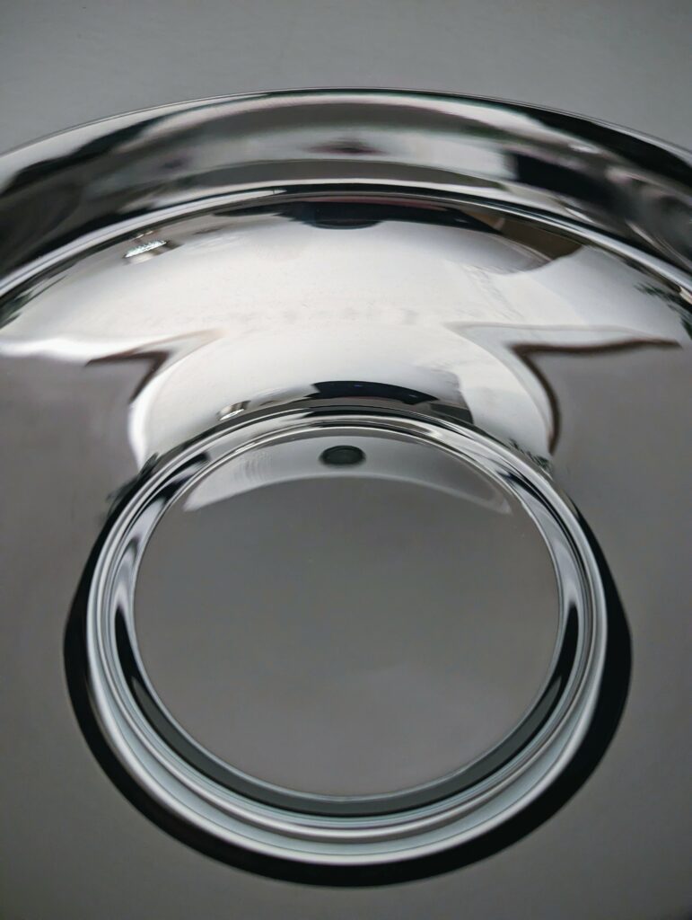 Close-up of a highly polished metal bowl, showing distorted grey and white reflections on its smooth, curved surface.