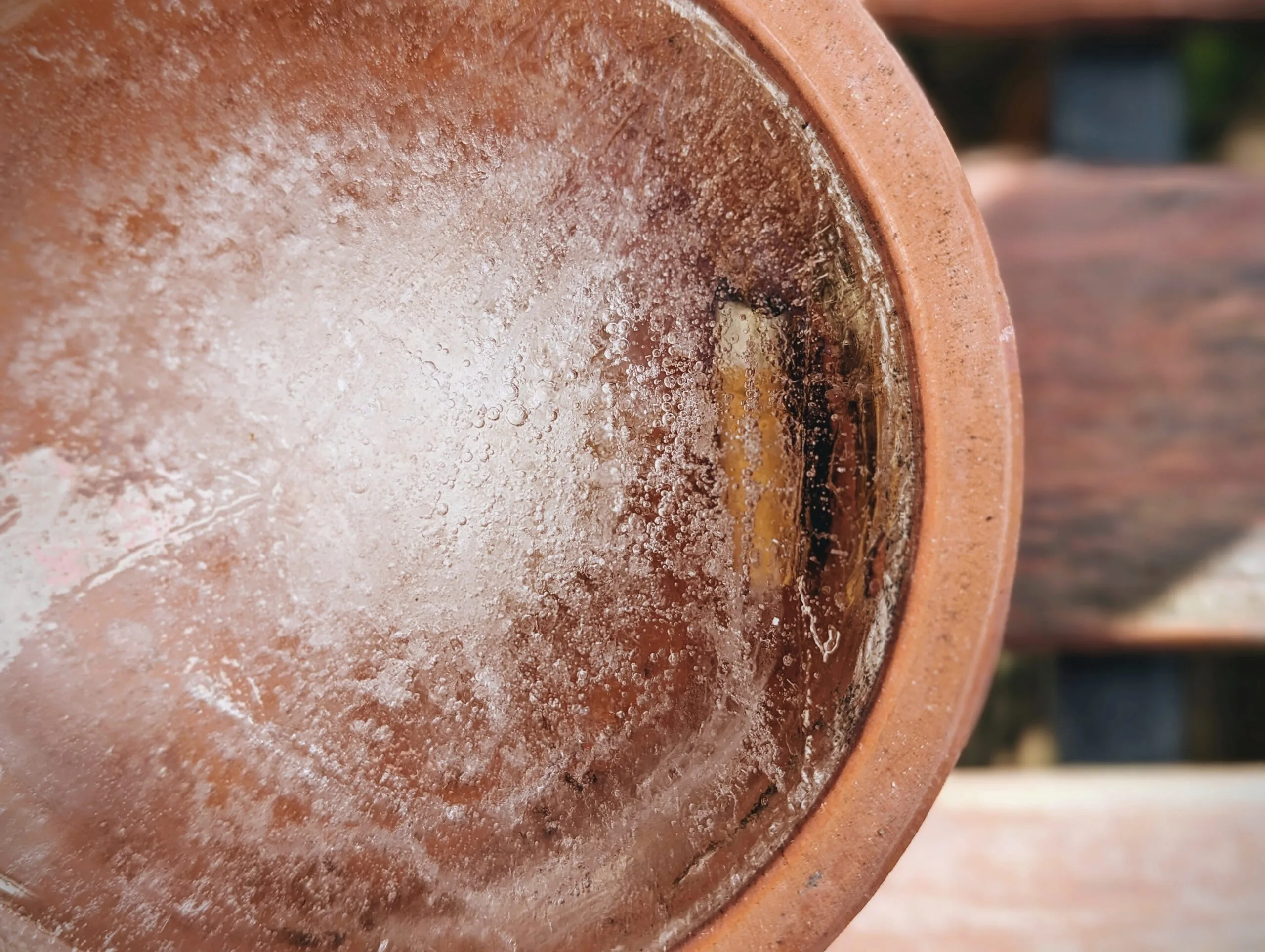 Textured frozen ice with many small trapped air bubbles inside a round terracotta pot saucer.
