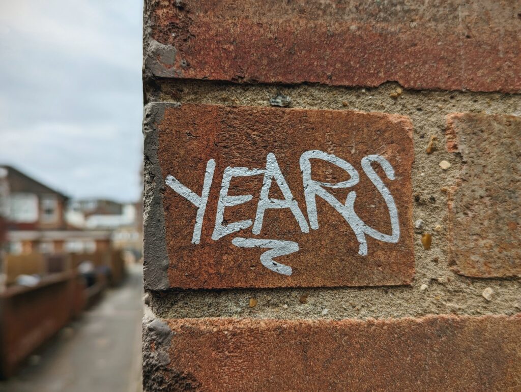 The word YEARS tagged in white paint on a red brick wall, with a blurred residential street in the background.