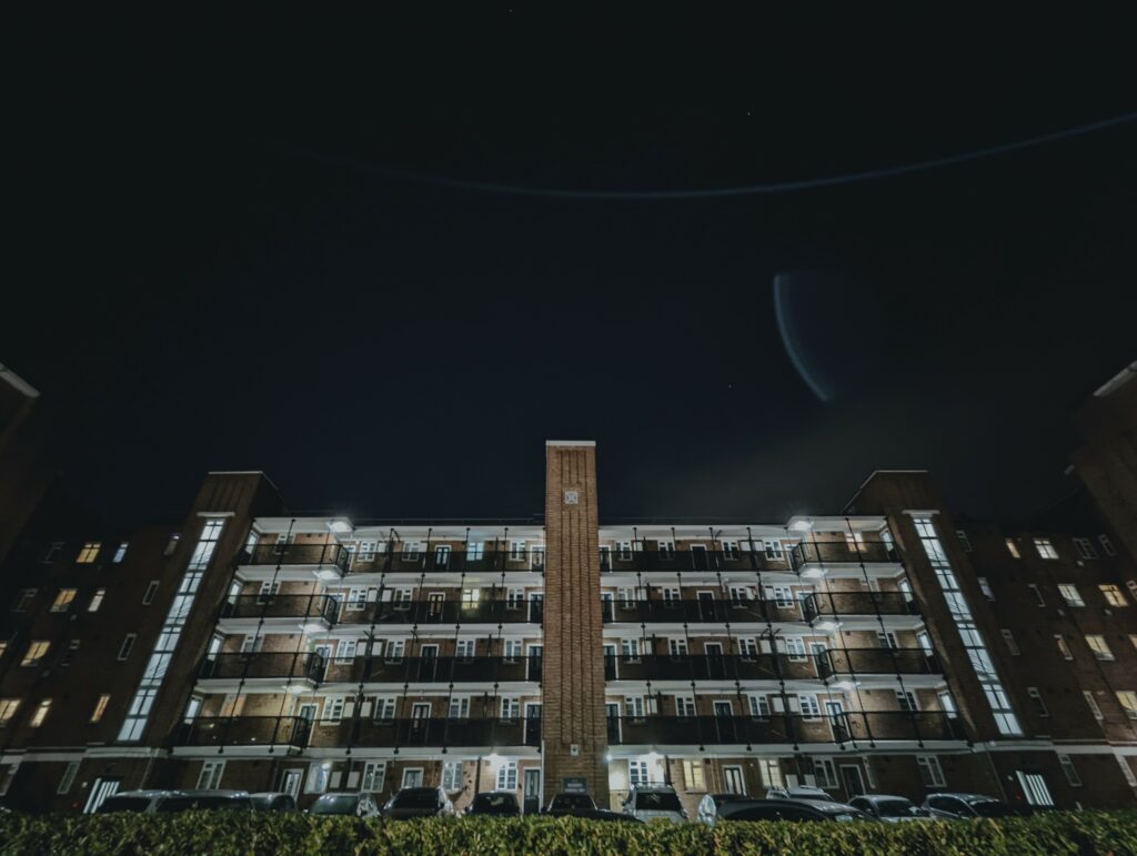 Symmetrical low-angle view of a brick apartment block at night with illuminated balconies and windows against a dark sky.