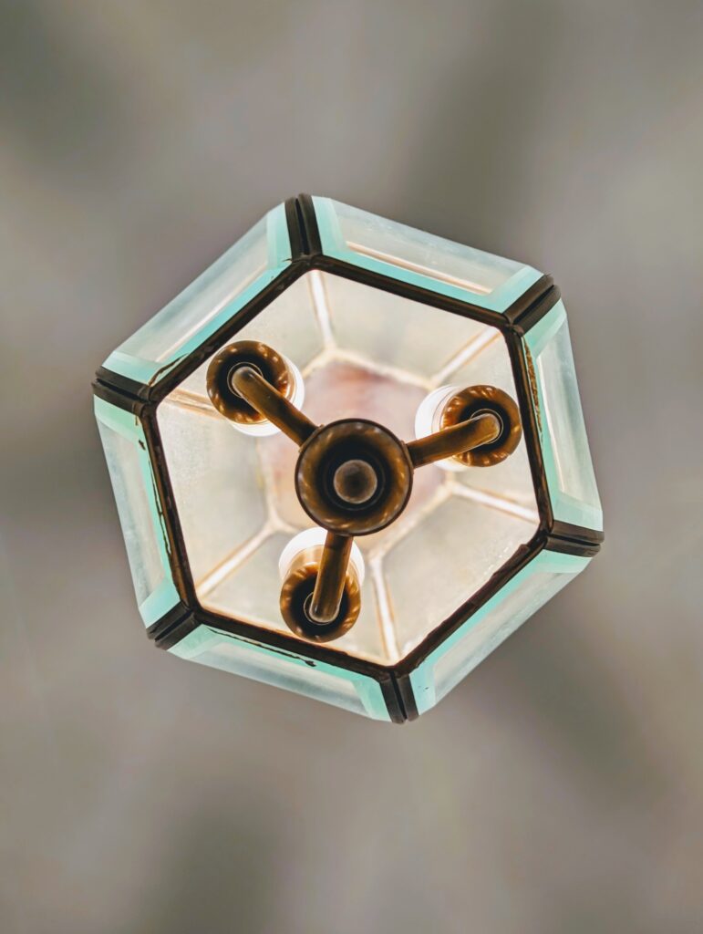 Low angle shot looking up into a hexagonal glass lantern with three internal brass arms and glowing light bulbs.