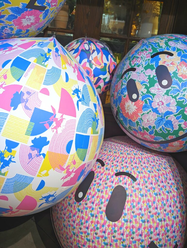 Vibrant inflatable balls with floral and geometric patterns, some featuring cartoonish smiley faces, stacked together in a colorful indoor display.