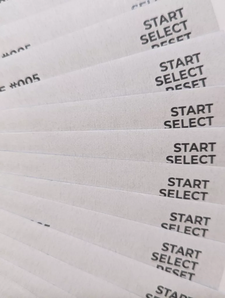 Close-up of white cards fanned out, each printed with the words START, SELECT, and RESET in a simple black sans-serif font.