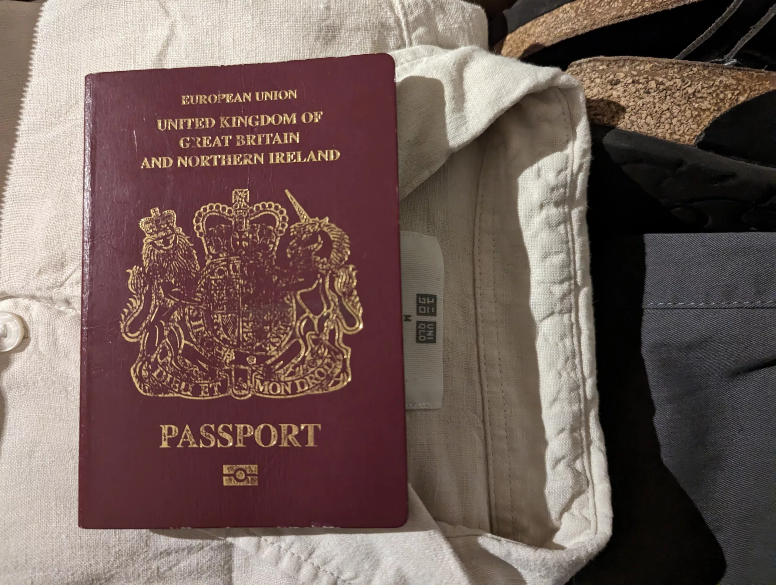 A burgundy European Union United Kingdom passport resting on top of a cream linen shirt and dark sandals.