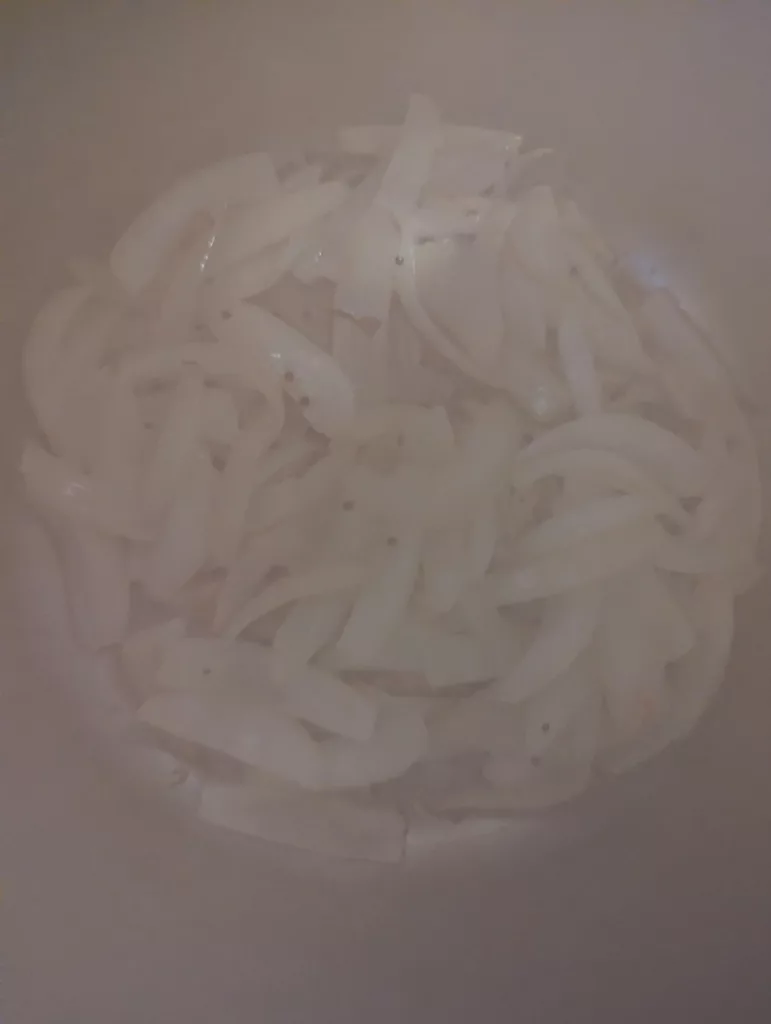 White onion slices sweating in a pan, partially hidden by a hazy layer of steam.