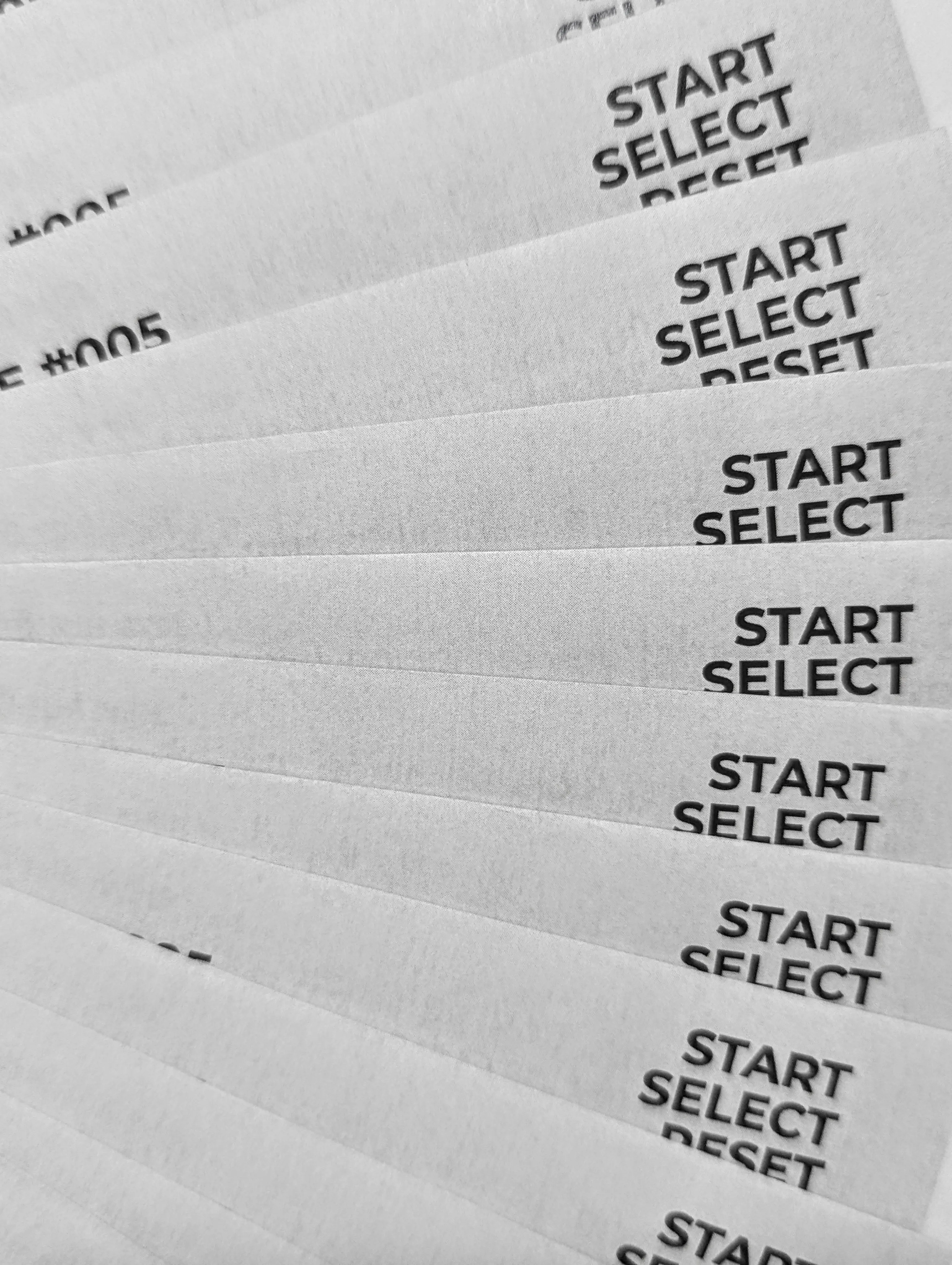 A black and white close-up of a fanned stack of papers printed with the words START, SELECT, and RESET in a bold sans-serif font.