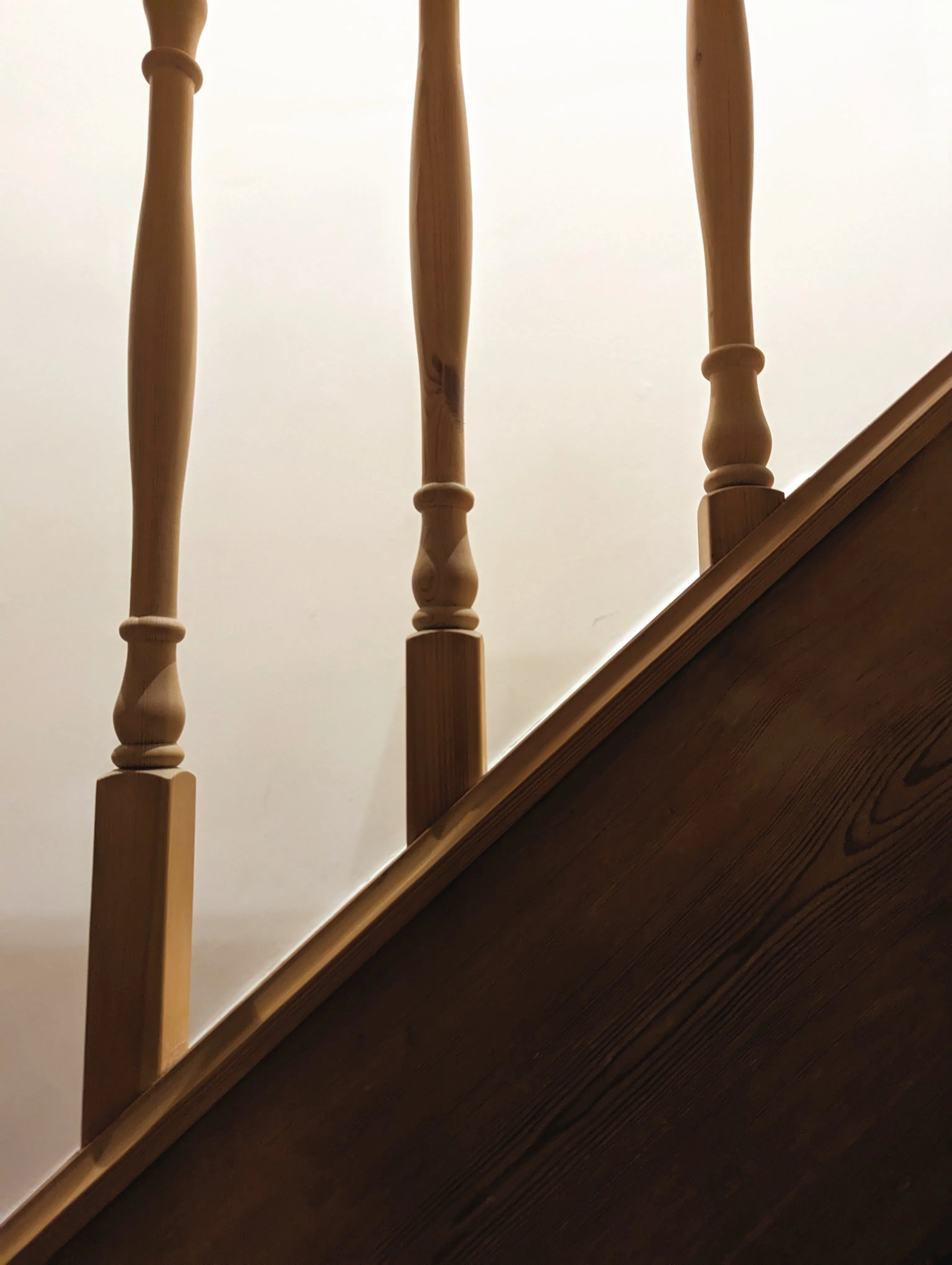 Three turned wooden staircase spindles silhouetted against a bright, softly lit interior wall.