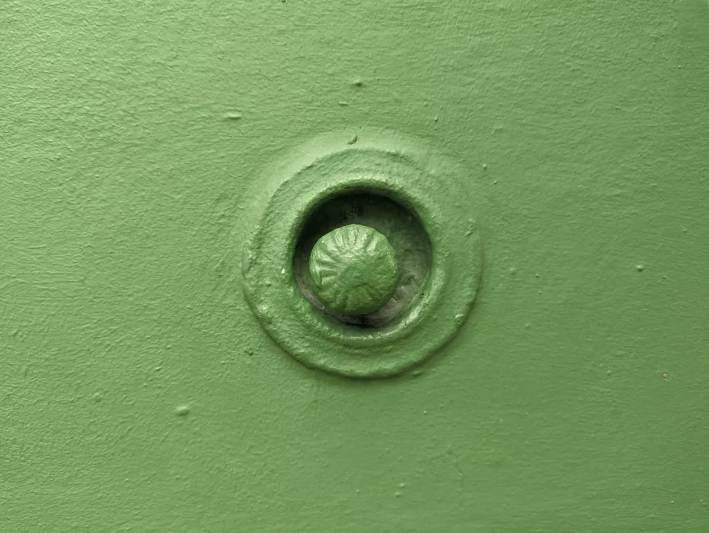 A textured green round knob set within a circular recess on a matching green painted wall.