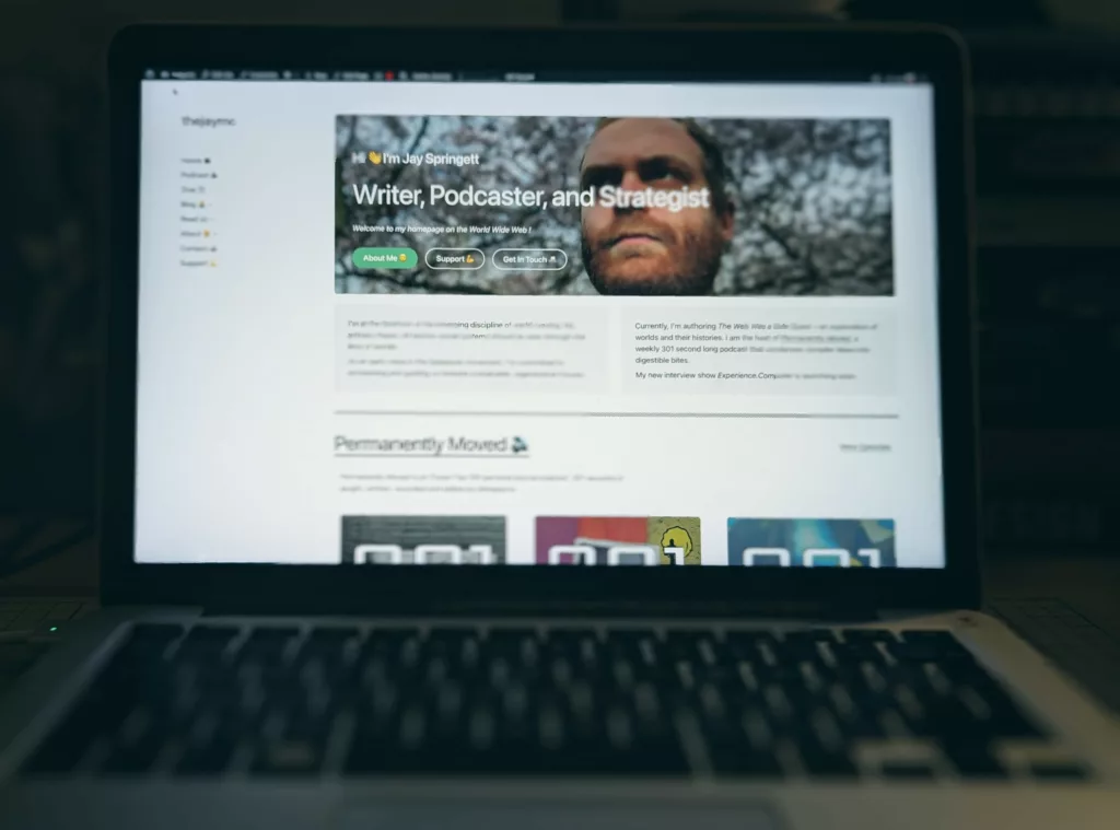 A laptop screen displaying the personal website of Jay Springett, featuring his portrait and the header: Writer, Podcaster, and Strategist.