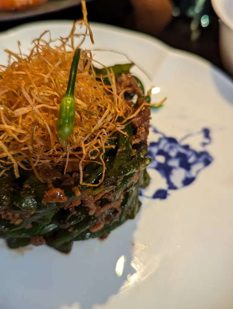 Dry-fried green beans with minced pork topped with a nest of crispy fried ginger on a white plate with a blue floral pattern.