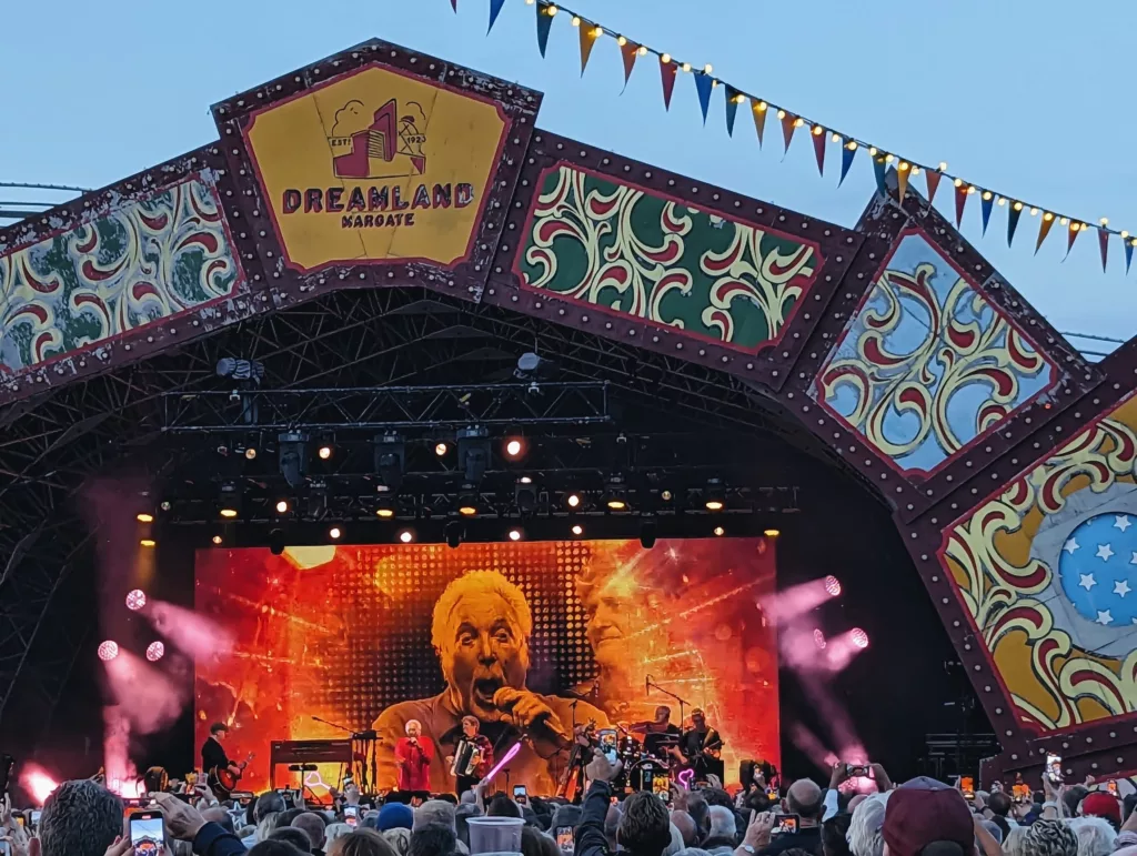 Tom Jones singing on a giant screen at the ornate Dreamland Margate stage, framed by colorful bunting and a concert crowd.