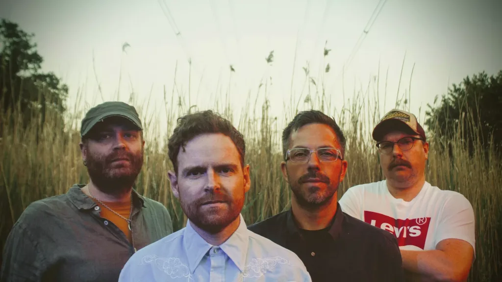 Forestbed band portrait - four men standing in front of tall reeds under a hazy sky.