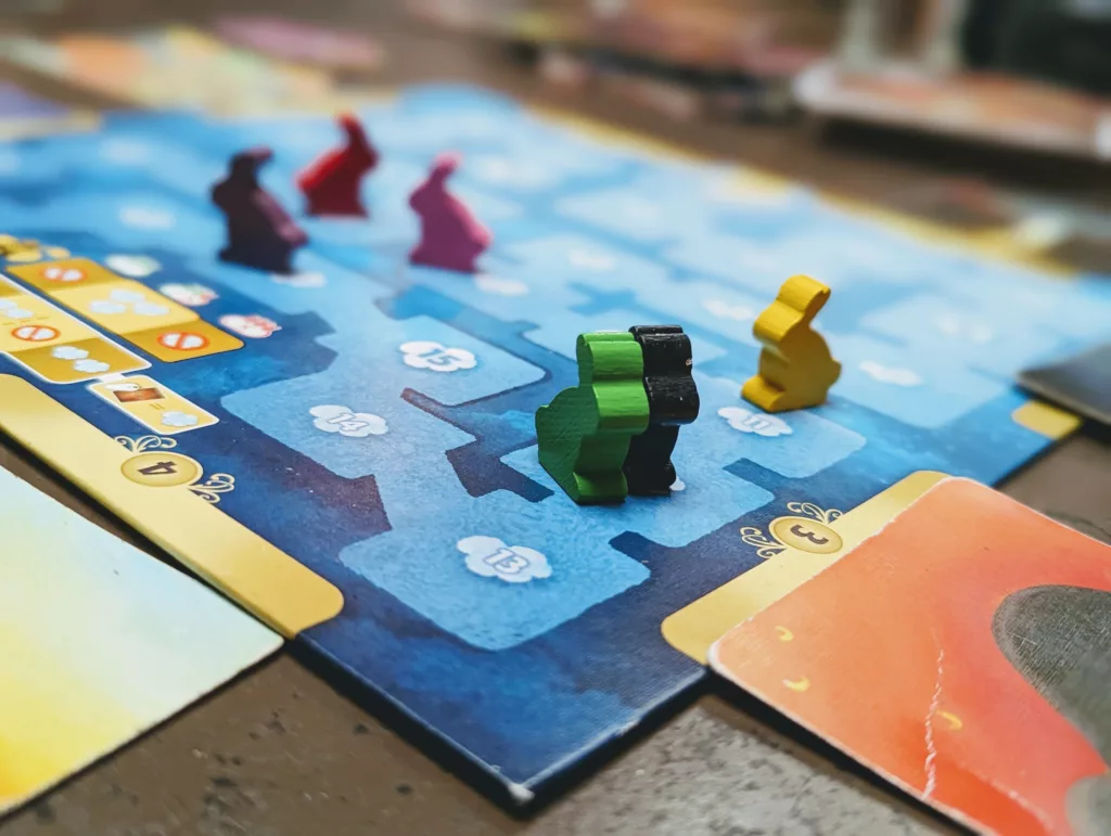 Colorful wooden bunny meeples on a blue Dixit board game scoring track. Green and black bunnies are in focus in the foreground.