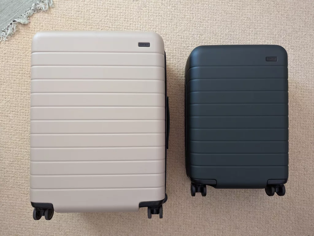 Two Away suitcases, one large beige and one smaller black carry-on, standing side-by-side on a tan carpet.