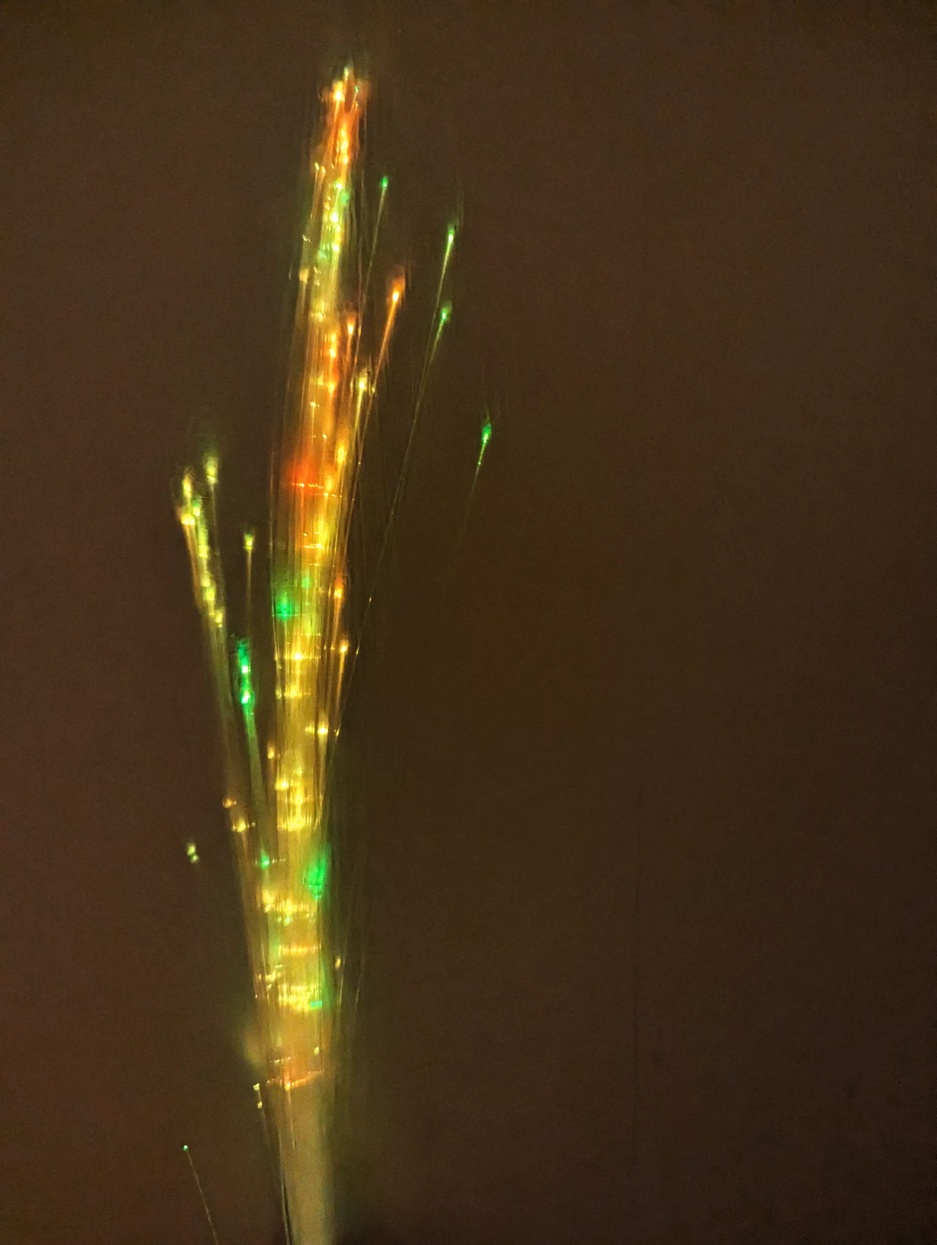 Vertical streaks of glowing green and orange light from a long exposure against a dark brown background.
