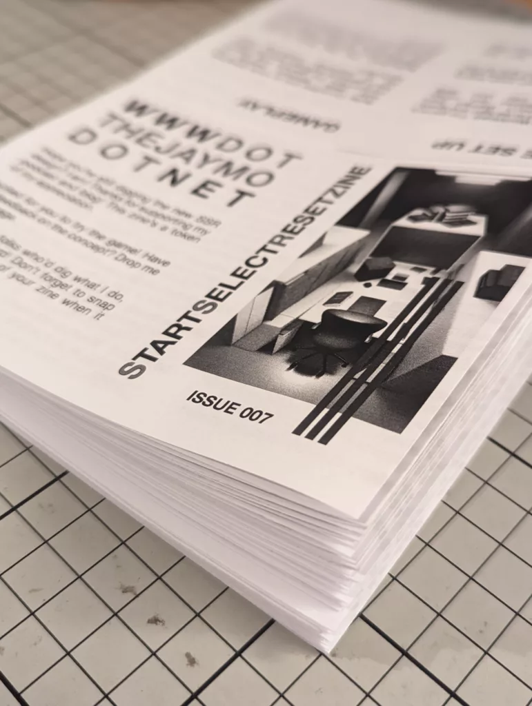 A thick stack of printed black and white zines titled StartSelectResetZine Issue 007, resting on a gridded cutting mat.