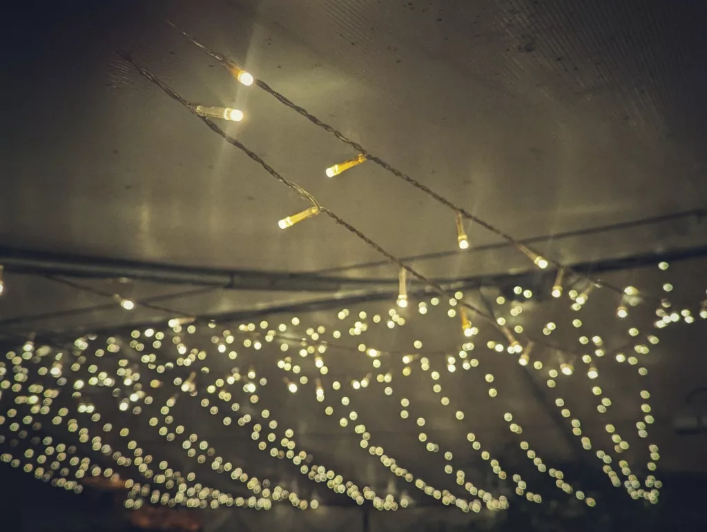 Warm fairy lights draped under a dark ceiling, with sharp foreground bulbs and background strings blurred into a soft bokeh.
