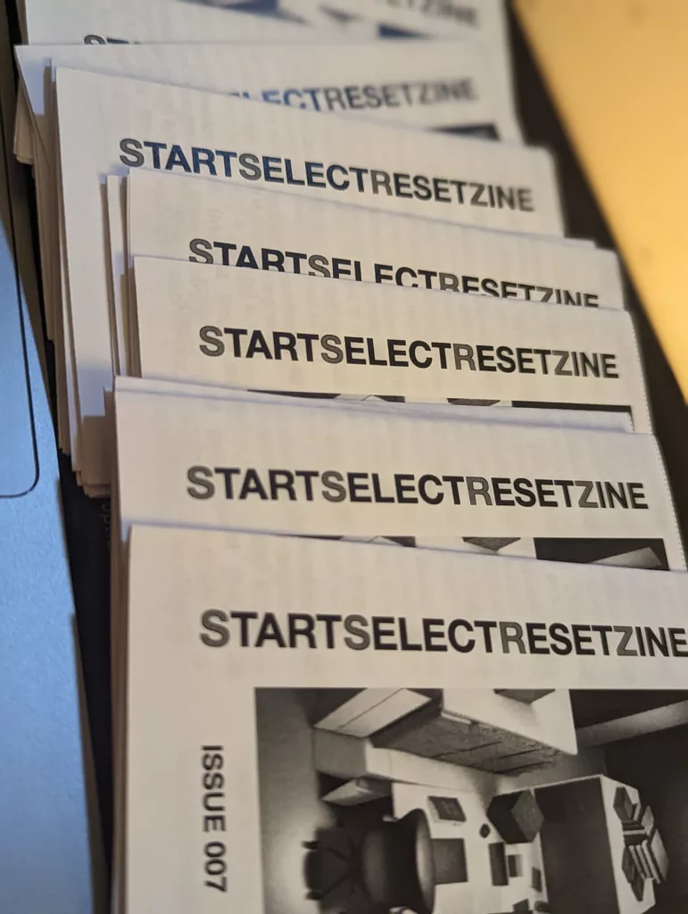 A stack of STARTSELECTRESETZINE Issue 007 fanned out, showing white covers with bold black titles and greyscale architectural illustrations.