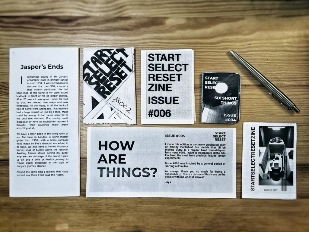 Monochrome mini-zines from the Start Select Reset series, issues #002 to #007, laid out on a wooden desk next to a silver ballpoint pen.