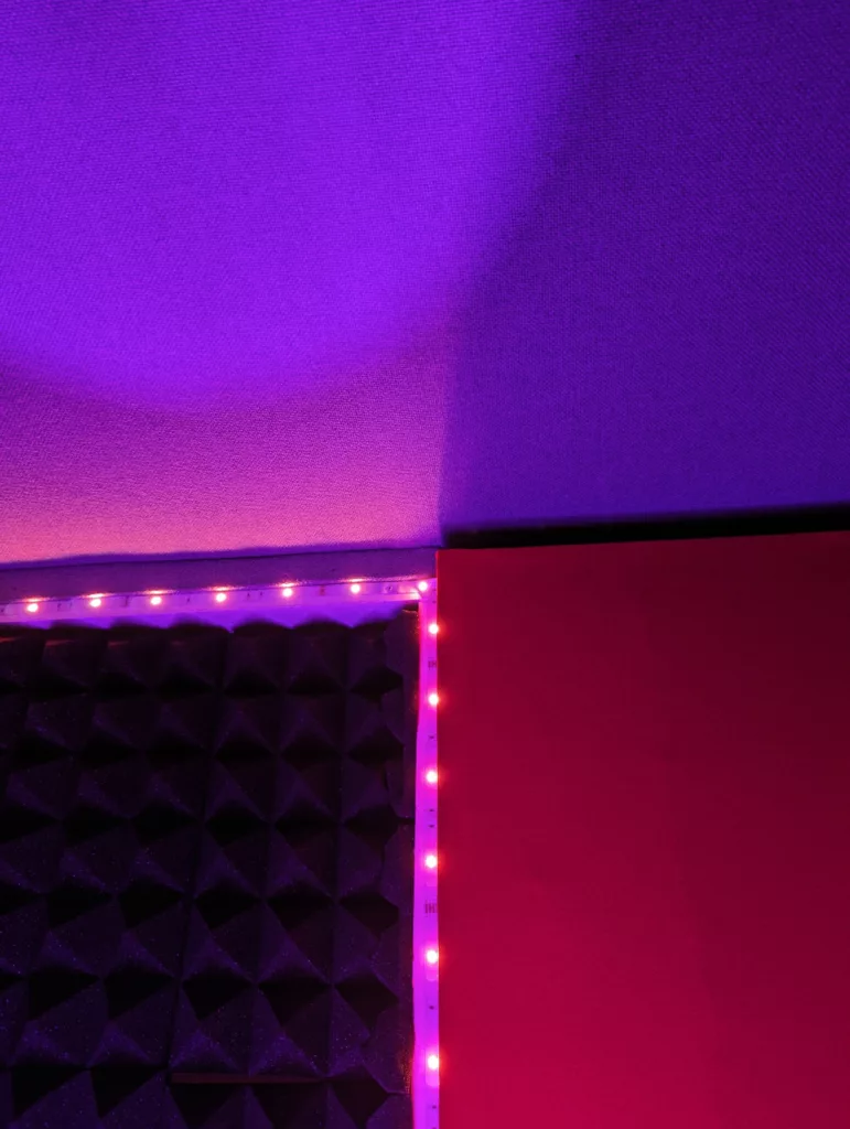 Pink LED strips bordering black acoustic foam and a red panel, casting a vibrant purple glow onto a textured ceiling.