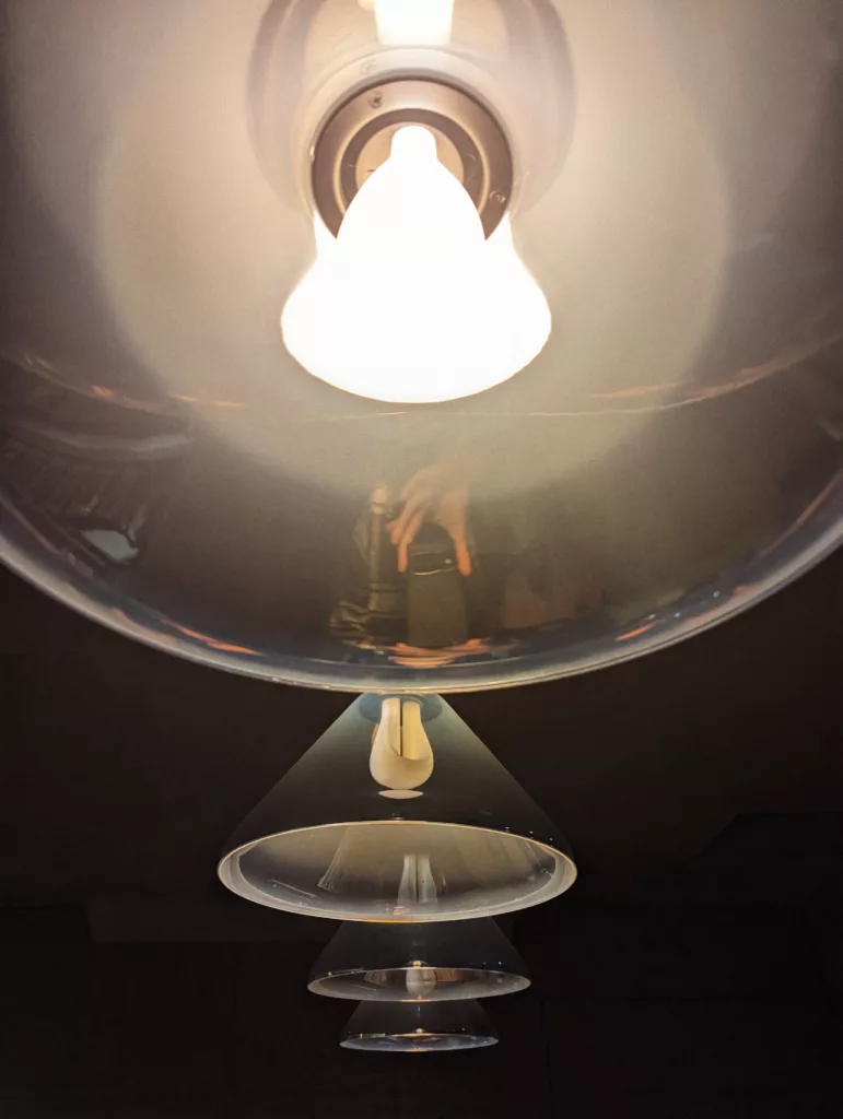 Looking up at a vertical row of four translucent dome pendant lights. The top light is glowing brightly against a dark background.