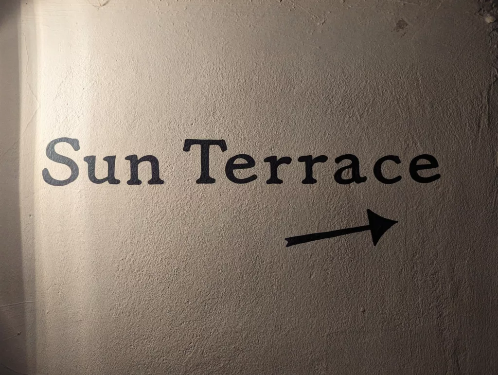 Sun Terrace text and a right-pointing arrow in black ink on a textured, beige wall under dramatic side lighting.