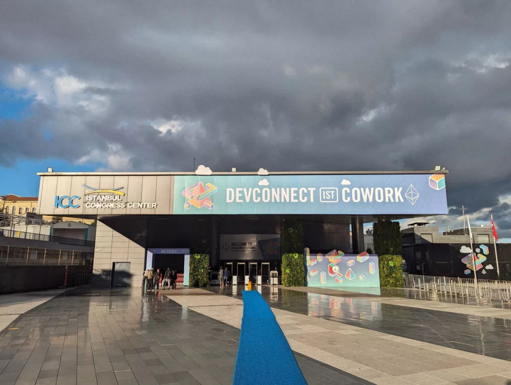 Devconnect IST Cowork banner at the Istanbul Congress Center with a long blue carpet on the ground under a dramatic, cloudy sky.