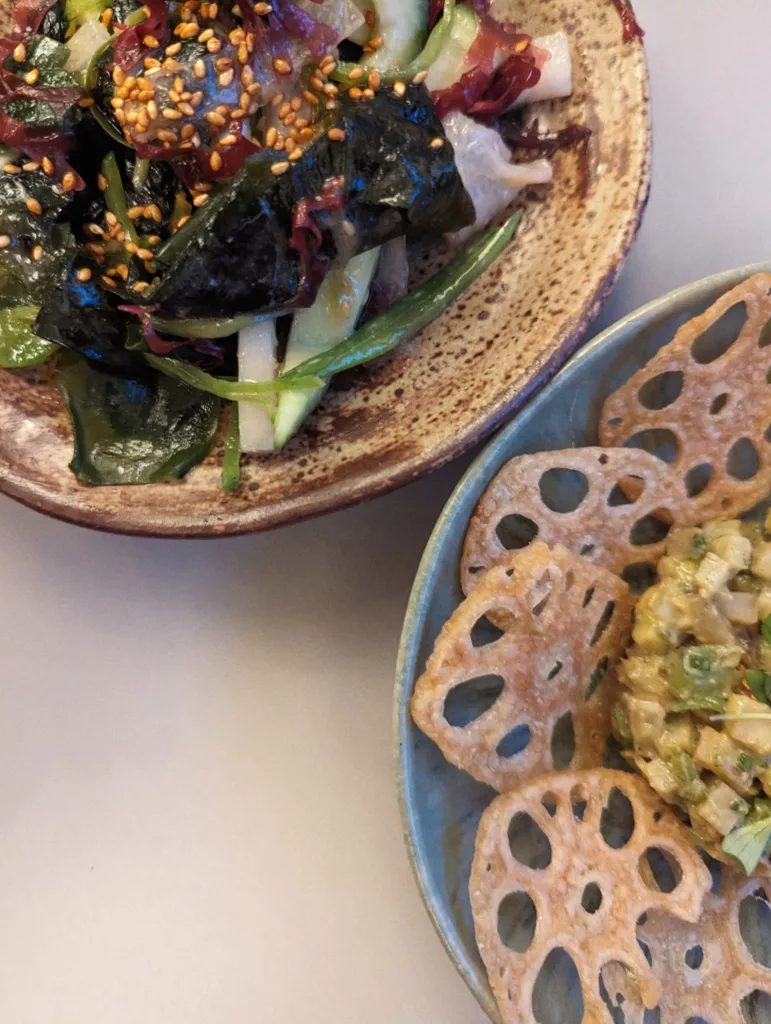 Seaweed salad with sesame seeds and cucumber slices beside a dish of crispy fried lotus root chips and a vegetable tartare.