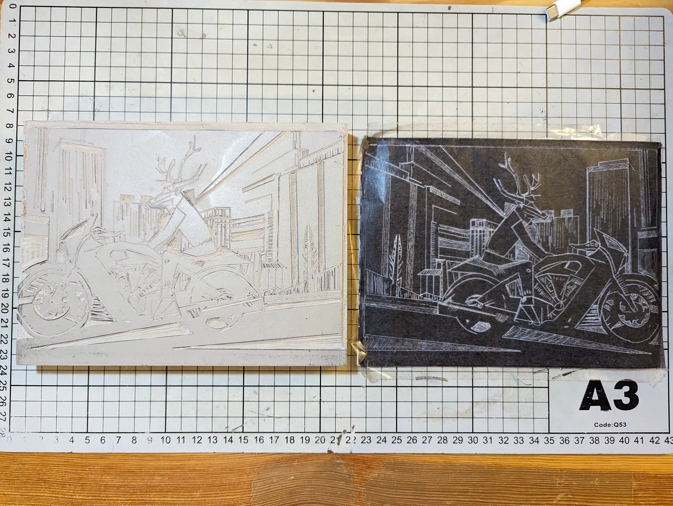A carved lino block and a black print showing a deer-headed figure riding a motorcycle through a city, laid out on a gridded A3 cutting mat.