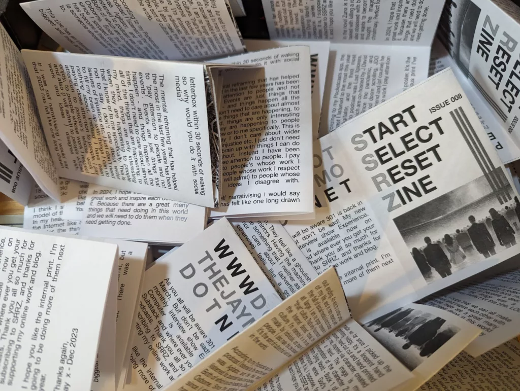 A scattered pile of black and white mini-zines titled Start Select Reset Issue 008, featuring dense text and grainy silhouette illustrations.