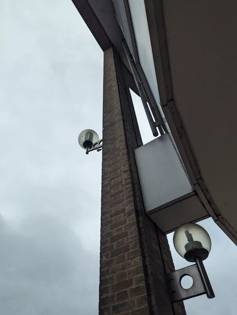 Spherical globe lamps on industrial metal brackets attached to a tall brick pillar under an overcast grey sky.