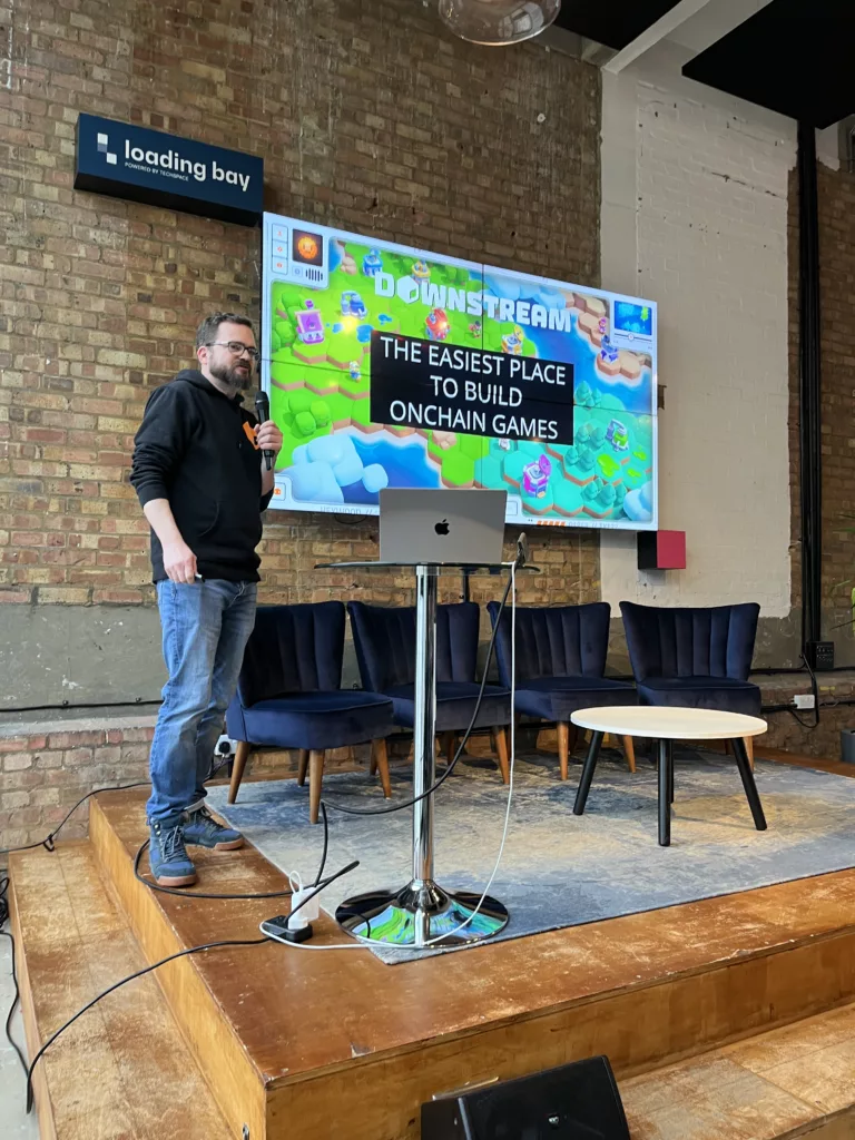 A man presents at Loading Bay. Behind him, a screen reads "Downstream: The easiest place to build onchain games" over a colorful game world.